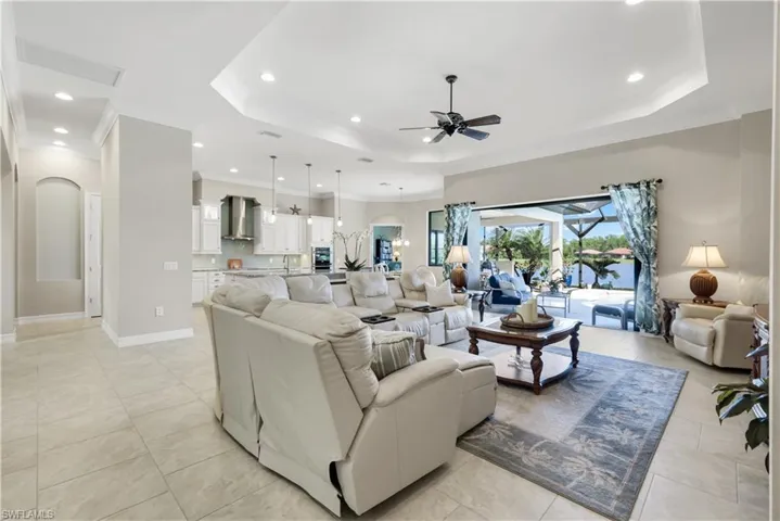 Living area featuring a tray ceiling, arched walkways, ornamental molding, recessed lighting, and ceiling fan