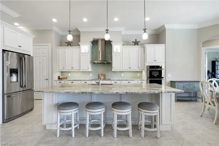 Kitchen featuring stainless steel appliances, light stone countertops, white cabinets, crown molding, and a breakfast bar
