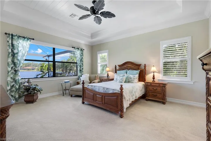 Bedroom with a raised ceiling, light colored carpet, crown molding, and ceiling fan