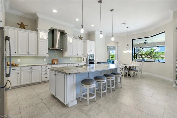Kitchen with light stone counters, ornamental molding, backsplash, stainless steel appliances, and wall chimney exhaust hood