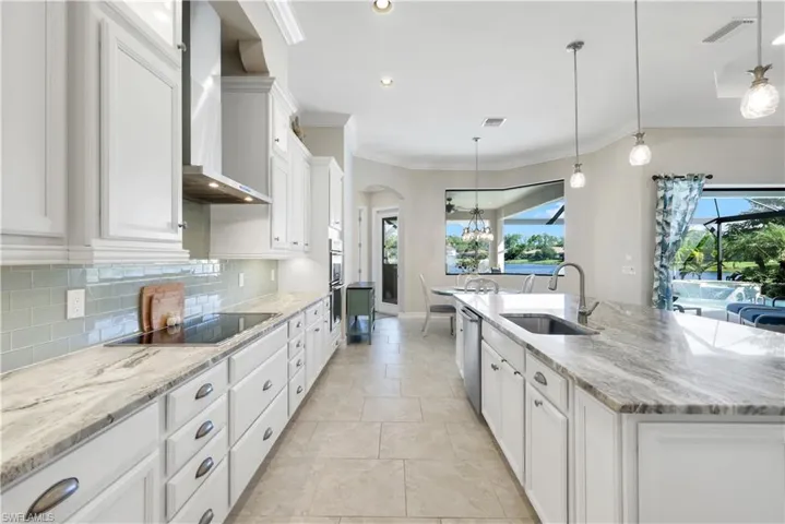Kitchen featuring white cabinets, light stone countertops, wall chimney range hood, decorative light fixtures, and recessed lighting