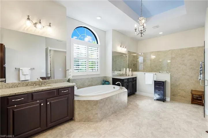 Full bath featuring a bath, a walk in shower, two vanities, light tile patterned floors, and a chandelier