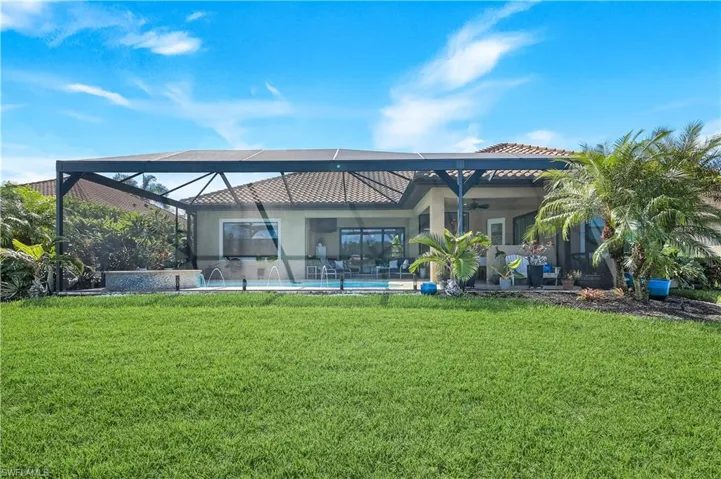 Rear view of property with a ceiling fan, a lawn, glass enclosure, and an outdoor pool