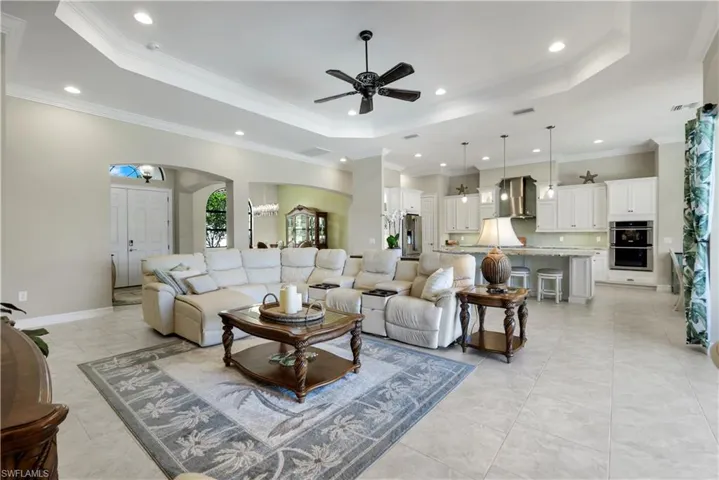 Living room with a raised ceiling, ornamental molding, recessed lighting, ceiling fan, and arched walkways