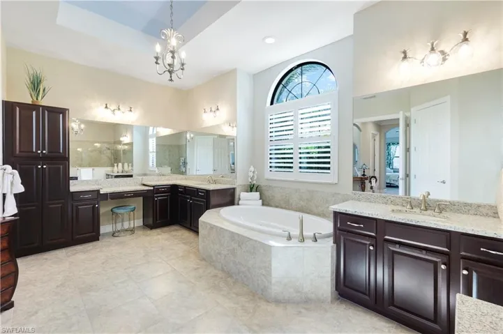 Bathroom featuring two vanities, a garden tub, a chandelier, and light tile patterned floors