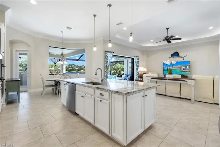 Kitchen featuring white cabinets, ornamental molding, light stone counters, decorative light fixtures, and a center island with sink