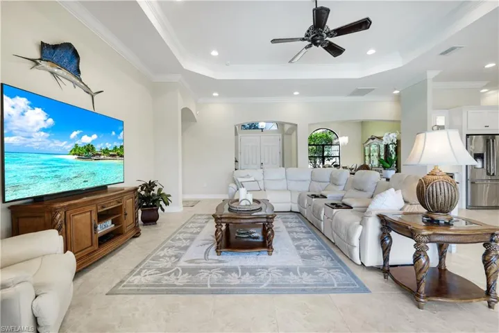 Living room featuring a raised ceiling, crown molding, arched walkways, ceiling fan, and recessed lighting