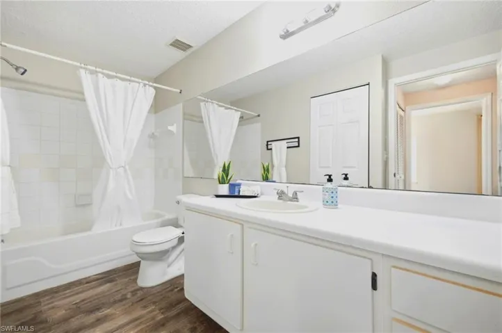 Full-width vanity with solid-surface countertop and integrated sink, expansive wall-mounted mirror, tub-shower combination with tile surround, and wood-finish flooring
