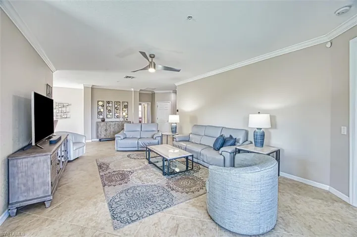 Living room featuring ceiling fan, crown molding, and light tile patterned floors