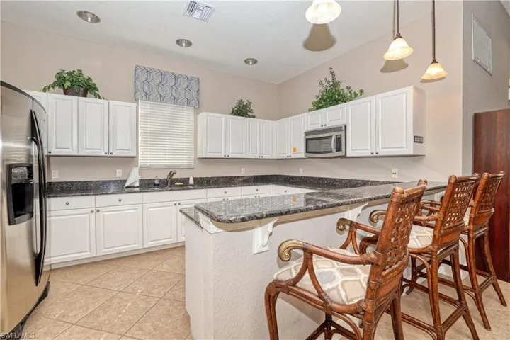 Clubhouse Kitchen with white cabinets, appliances with stainless steel finishes, decorative light fixtures, kitchen peninsula, and a breakfast bar area