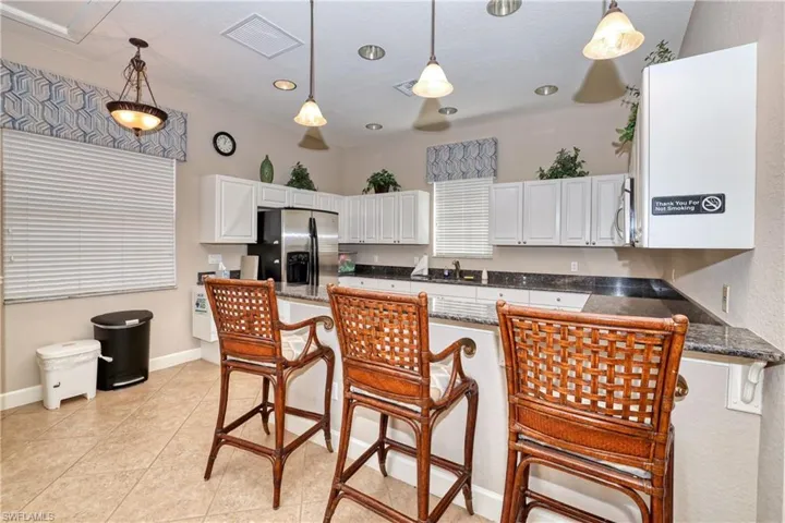 Clubhouse Kitchen with a kitchen bar, appliances with stainless steel finishes, light tile patterned floors, pendant lighting, and white cabinets