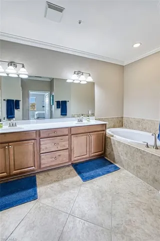 Bathroom featuring tile patterned flooring, vanity, ornamental molding, and tiled tub