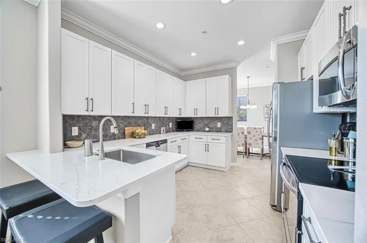 Kitchen featuring kitchen peninsula, appliances with stainless steel finishes, a kitchen breakfast bar, decorative light fixtures, and white cabinets