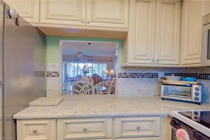 Kitchen with stainless steel appliances, light stone countertops, cream cabinetry, tasteful backsplash, and ceiling fan