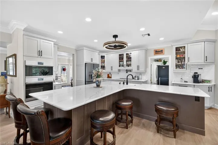 Kitchen with a breakfast bar area, glass fronted cabinets, a spacious island, recessed lighting, and ornamental molding