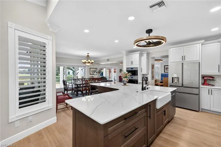 Dual tone kitchen featuring ornamental molding, dual tone cabinets, stainless steel refrigerator with ice dispenser, a center island with sink, Quartz Counters