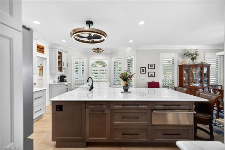 Kitchen featuring a spacious island, light stone countertops, dual tone cabinets, a warming drawer, and glass insert cabinets