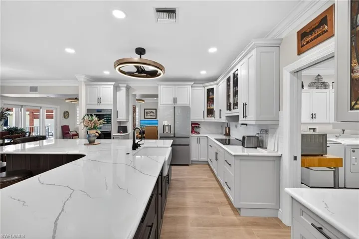 Kitchen with ornamental molding, glass fronted cabinets, two tone color scheme, Quartz counters, and recessed lighting