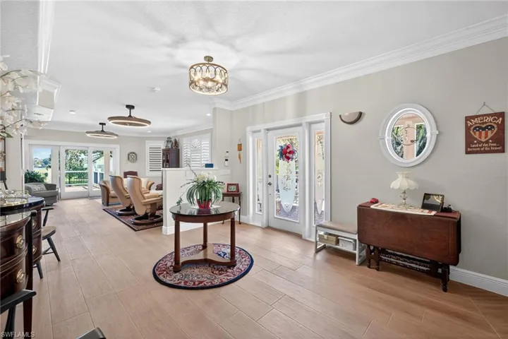 Foyer entrance featuring crown molding, light wood-type flooring, and suspended lighting