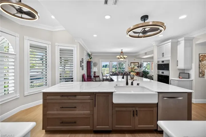 Kitchen with two tone cabinets, suspended lighting, stainless steel appliances, a center island with sink, and light wood-type flooring