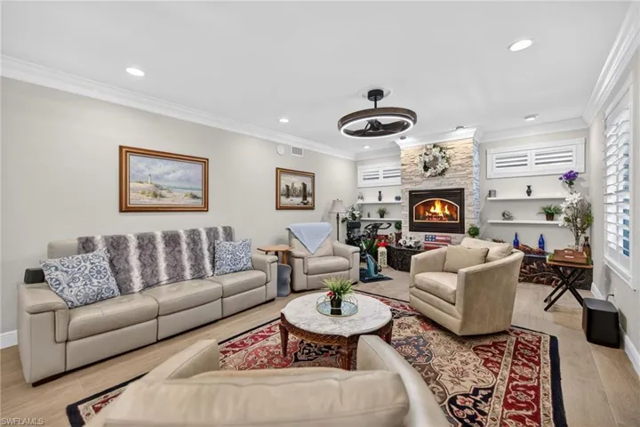 Living room with light wood-style floors, ornamental molding, ceiling fan, a large fireplace, and recessed lighting