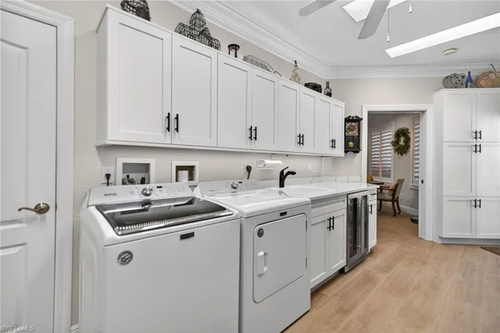 Laundry area featuring ornamental molding, beverage cooler, cabinet space, washing machine and dryer, and light wood-style floors