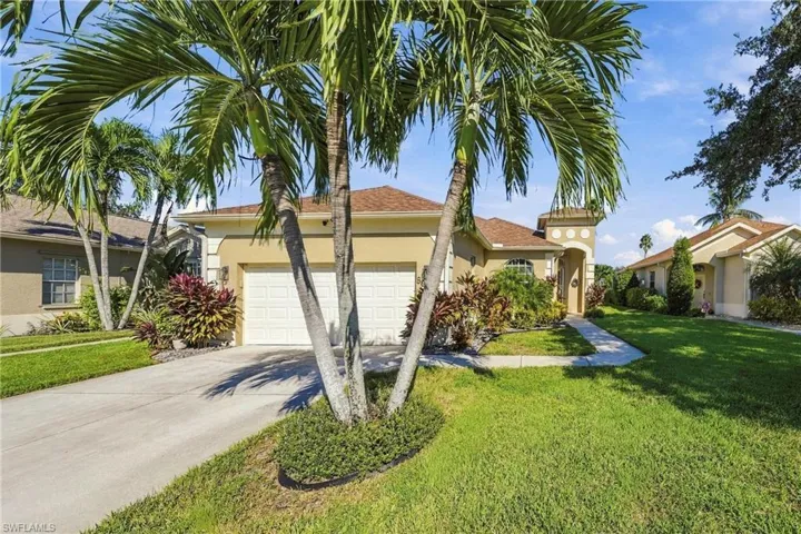 Single-story residence featuring a stucco exterior, concrete driveway, two-car garage, manicured lawn, and mature palm trees