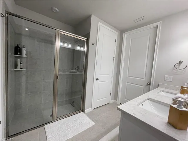 Bathroom with double vanity, light tile patterned floors, and a stall shower