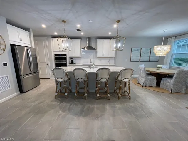 Kitchen with pendant lighting, stainless steel appliances, white cabinetry, recessed lighting, and wall chimney exhaust hood