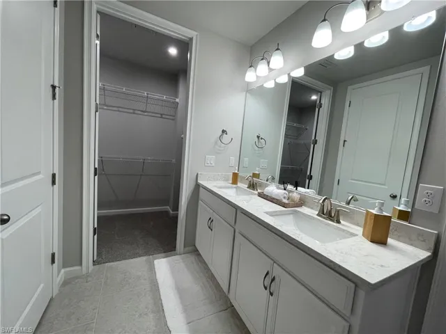 Bathroom featuring a walk in closet, double vanity, and light tile patterned floors