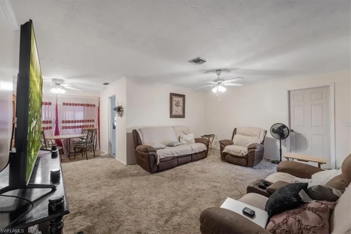 Carpeted living area with ceiling fan, ornamental molding, and a textured ceiling