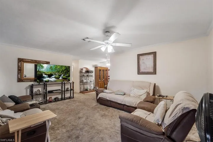 Living area featuring carpet floors, crown molding, and ceiling fan