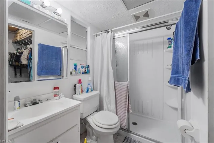 Full bath with a textured ceiling, a stall shower, vanity, and a spacious closet