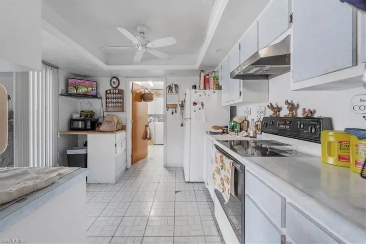 Kitchen with electric stove, a raised ceiling, under cabinet range hood, a ceiling fan, and light countertops