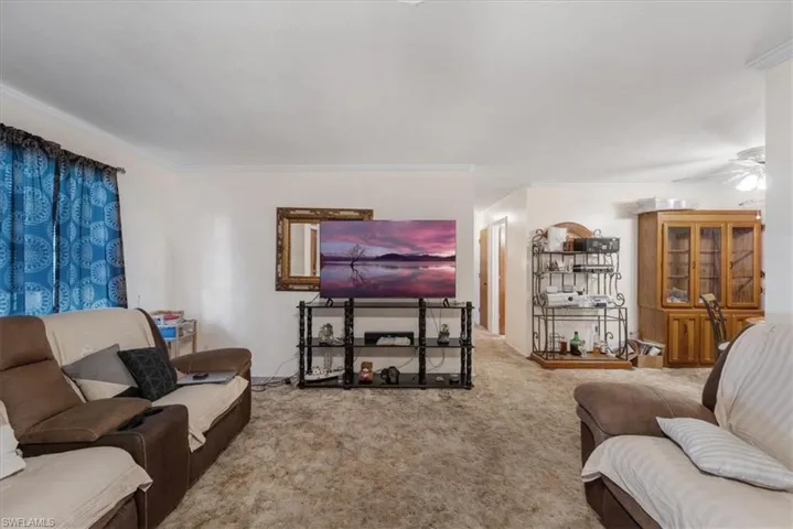 Carpeted living area featuring crown molding and a ceiling fan