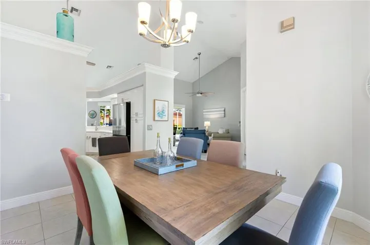 Dining area with ceiling fan with notable chandelier, light tile patterned flooring, crown molding, and high vaulted ceiling