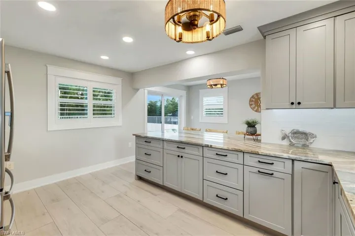 Kitchen with recessed lighting, light stone counters, light wood-style flooring, a peninsula, and gray cabinets