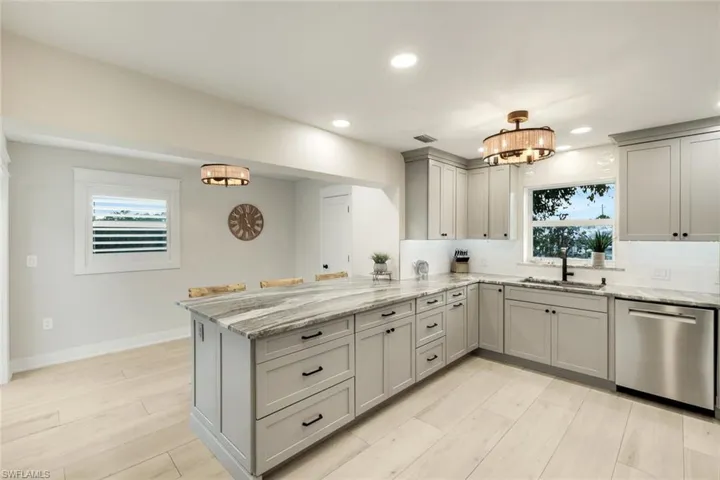 Kitchen with gray cabinetry, a peninsula, dishwasher, and light stone counters