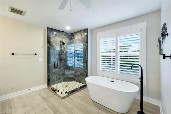 Bathroom with a marble finish shower, a freestanding tub, light wood-style floors, and ceiling fan
