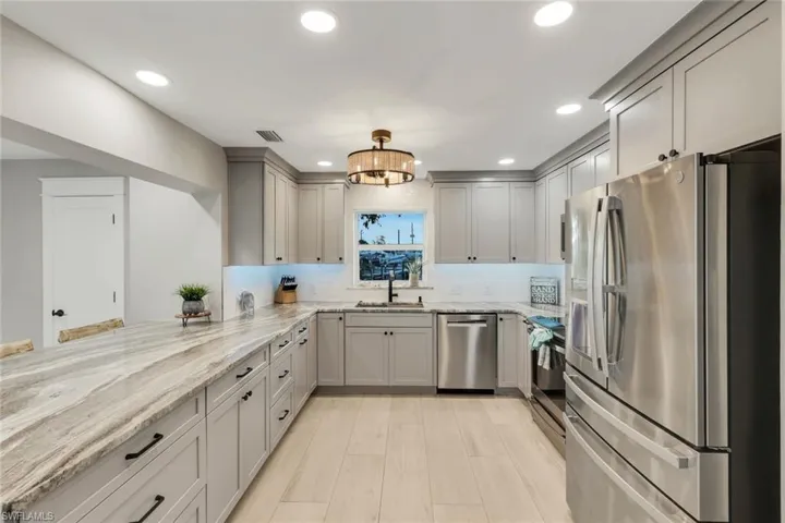 Kitchen with stainless steel appliances, light stone countertops, light wood finished floors, a peninsula, and gray cabinets
