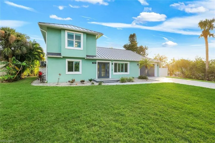 View of front of home with a standing seam roof, stucco siding, driveway, and a front yard