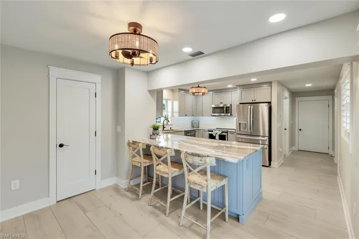 Kitchen with light stone counters, stainless steel appliances, a kitchen breakfast bar, a peninsula, and light wood-style flooring