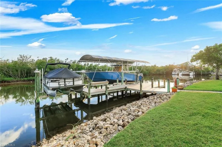 Dock featuring boat lift, a water view, and a yard