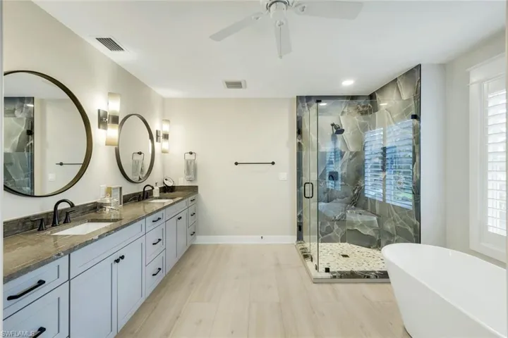 Bathroom featuring double vanity, a marble finish shower, a freestanding bath, light wood-style flooring, and ceiling fan