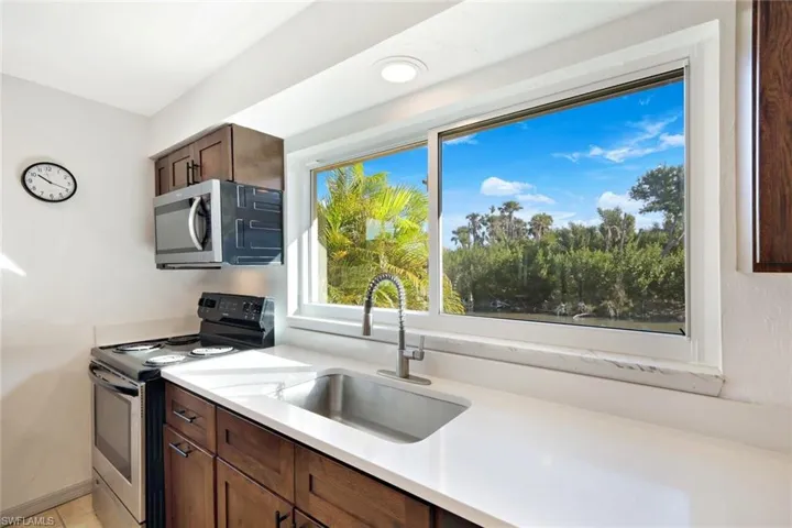 Kitchen featuring stainless steel appliances, dark brown cabinets, and light stone counters