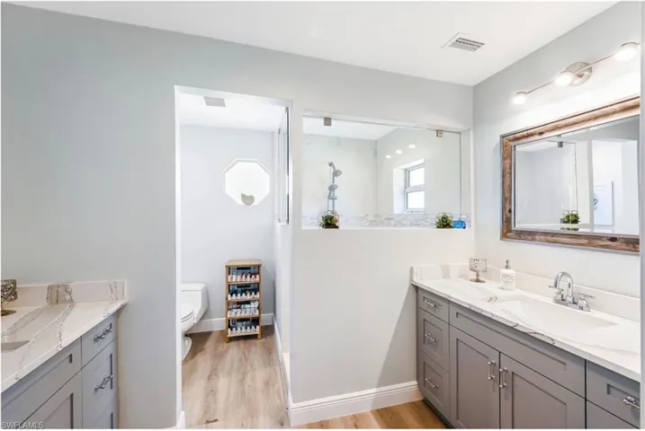 Full bath featuring toilet, wood finished floors, and two vanities