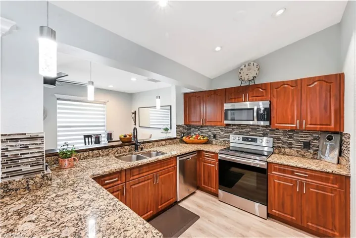 Kitchen featuring stainless steel appliances, a sink, light stone countertops, tasteful backsplash, and vaulted ceiling