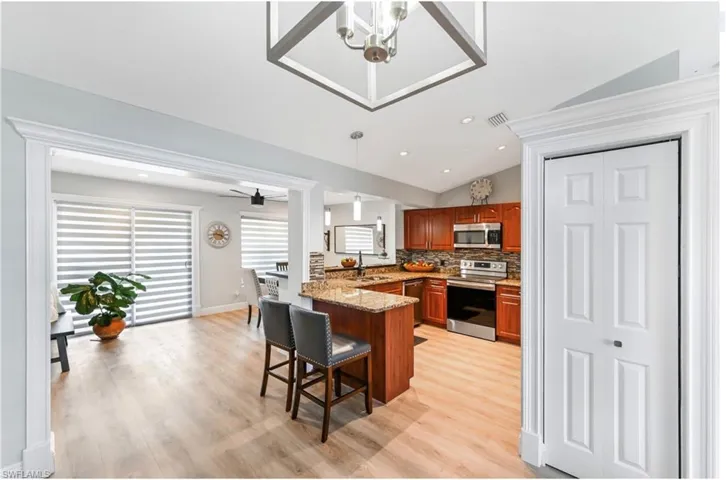 Kitchen featuring stainless steel appliances, vaulted ceiling, brown cabinetry, a peninsula, and a breakfast bar area