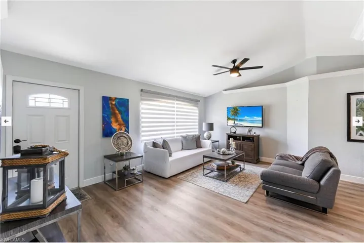 Living room featuring lofted ceiling, ceiling fan, wood finished floors, and baseboards