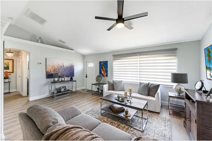 Living area with vaulted ceiling, ceiling fan, healthy amount of natural light, wood finished floors, and arched walkways